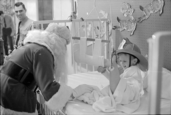 The Madison Firefighters' Union Local 311 Santa visiting the Methodist Hospital pediatrics ward for the annual Christmas party. Shown with Santa is Ricky Wells (6) wearing a fireman's helmet.