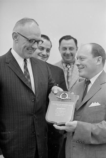 Sheriff Vernon Leslie, left, presenting an award to Richard Green, 1143 E. Dayton Street, for his part in the capture of Raymond Wyngaard, one of the FBI's 10 Most Wanted Men. Green was the cab driver who picked up Wyngaard at the train station and drove him to the east side where FBI agents captured him. Looking on during the Dane County Law Enforcement Officers Association presentation are Special Deputies James Coccitolo, chairman of the award committee, second from the left, and Andrew Drotin, secretary of the county association.