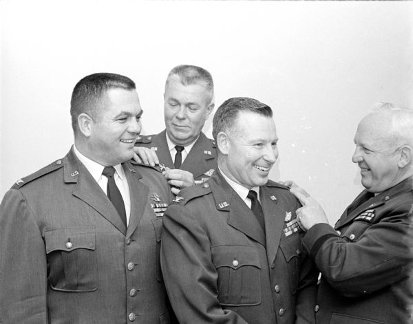 Two Wisconsin Air National Guard officers shown receiving promotions at a ceremony at the Truax Officers Club. Left to right: Col. Arlie Mucks, Jr., receiving his insignia from Maj. Gen. Collins Ferris, chief of staff of the Wisconsin Air National Guard; and Col. Thomas Moffatt, receiving his shoulder pin from Maj. Gen. Ralph Olson, adjutant general of the state of Wisconsin.