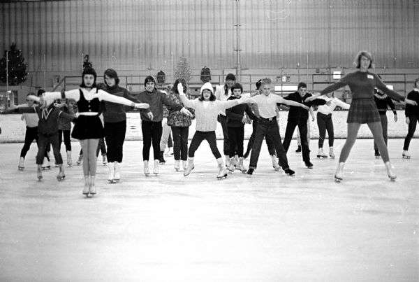 The Madison Figure Skating Club holding a free figure skating clinic for elementary school children and teenagers at the Madison Ice Arena, 1834 Commercial Avenue. Mrs. Gordon Sinykin is director of the clinic. Shown leading the figure skaters in a "fishtail forward" routine are Kim Borgatta (L) and Jackie Zoch (R).