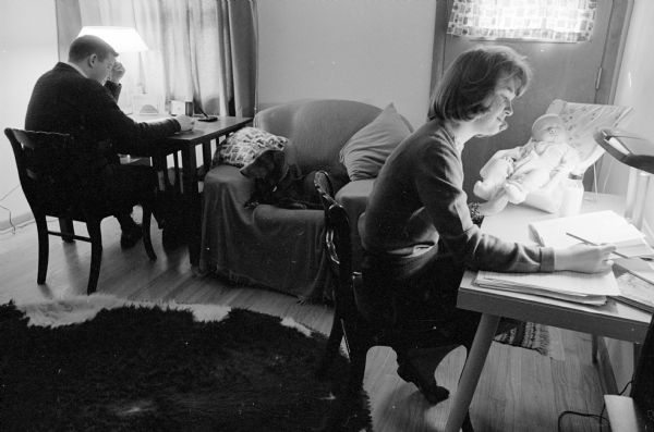 Gregory and Patty Herrling are shown studying in their apartment with their baby, Jimmy, in a car seat nearby. This was a typical evening while they worked on their U.W. degrees. They have now graduated, but will continue living in their apartment until they have the means to build a home in the country.