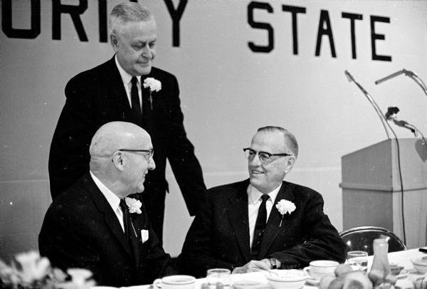 600 members attend the annual Security State Bank dinner at the East Side Business Men's Club to celebrate the 40 year anniversary of the  bank. Speakers shown, left to right, are: (seated) Leo L. Lunenschloss, bank founder and chairman of the bank board, and former Rep. Walter H. Judd (R-Minn); and (standing) Ray Sennett, bank president. 
