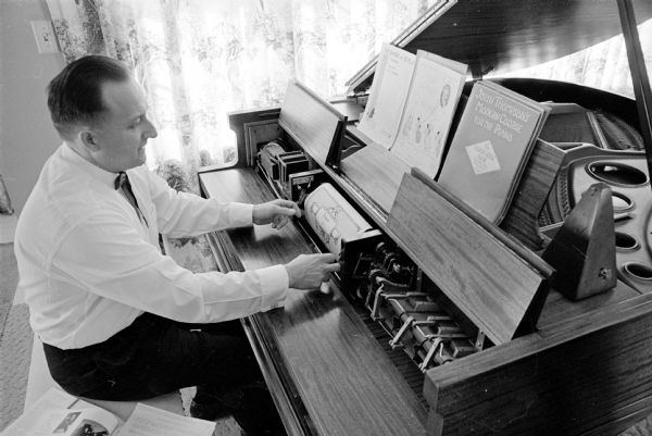 Chester Kuharski adjusting a roll on his reproducing piano. The Duo-Art piano performs in three ways — as a regular piano, a player piano, and as a reproducing piano. Chester is a WKOW radio transmitter engineer.