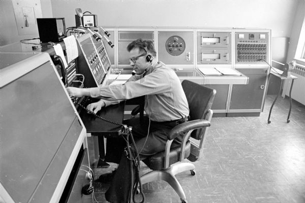 Dispatcher Sgt. L.E. Odegaard sitting at a switchboard surrounded by newly installed dispatching equipment. Odegaard is on the second floor of No. 3 station, 1217 Williamson Street. The dispatchers' room was moved from No. 1 station, 18 S. Webster Street, to the Williamson Street fire station because it was fire resistant and would help lower Madison's fire insurance rates.