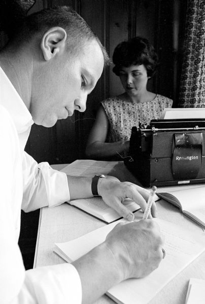 Donna Osness typing a paper for her husband, Wayne, foreground, who is a University of Wisconsin Ph.D student. One of a series of images about Donna, a mother of five children, who is participating in a new Madison General School of Nursing program for married women.