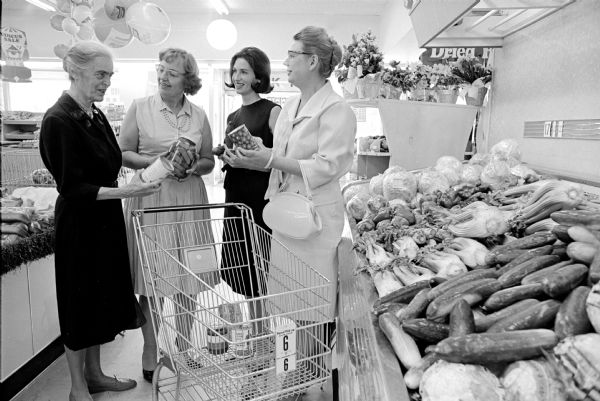 Four women interested in migrant workers are shown examining foods picked annually by migrants. They will participate in a meeting sponsored by Covenant Presbyterian Church to discuss aid for migrant workers. They are: Elizabeth Raushenbush, chairman of the governor's committee on migratory labor; Jenny Lind, State Department of Public Welfare; Marylu Raushenbush, chairman of the church association's program committee; and Margaret Salick, a migrant worker consultant.