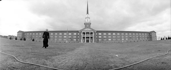 Panoramic view of Msgr. George Wirz strolling in front of the new Colonial-style Holy Name Seminary.