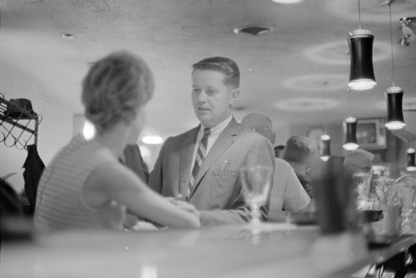 Two unidentified individuals (man and woman) discuss a beverage tax proposed by the state legislature. The man may be Edwin Jones?