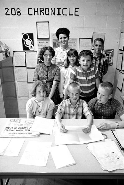 Seven Schenk School students of room 208 with their teacher, shown in front of a table covered with newspapers. They have produced their own class newspaper, "208 Chronicle." Seated, left to right, are Mary Nofsinger, Mike Fosdick and Kevin Morissey. Standing are Stacia Johnson, Teacher JoAnne McGinnity, Karin Olson, John Kitto and Dave Brockman.
