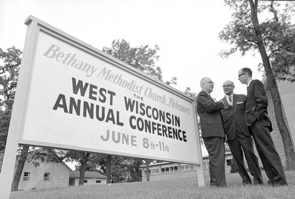 Three men standing next to large sign with the words "Bethany Methodist Church Welcomes the West Wisconsin Annual Conference June 8th-11th. Left to right are Rev. Gomer Finch, Wisconsin Bishop Ralph Alton, and Rev. Billy Bross. Finch and Bross are pastors of Bethany Church, located at 3910 Mineral Point Rd.
