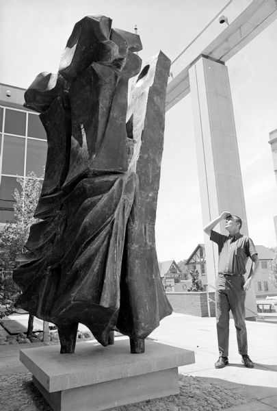 Passerby looking at "Heiroglyph," a sculpture made by O.V. Shaffer, Beloit, located in front of the new Madison Public Library, 201 West Mifflin Street. The front of the sculpture is supposed to suggest canyon walls and caves on which man first recorded painting and hieroglyphics.