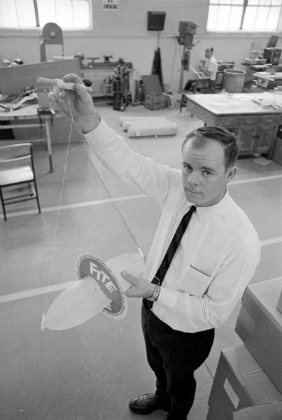 Pat Kohl is holding a new kite being manufactured by Madison Opportunity Center, a rehabilitation workshop for the mentally and physically handicapped. It has an 18-inch wing inserted through a red cardboard disc. It makes a fluttering noise and soars, maneuvers, and dog fights. The design was the idea of Leon H. Sweet who formed the "Fite Kite" company with four other men.