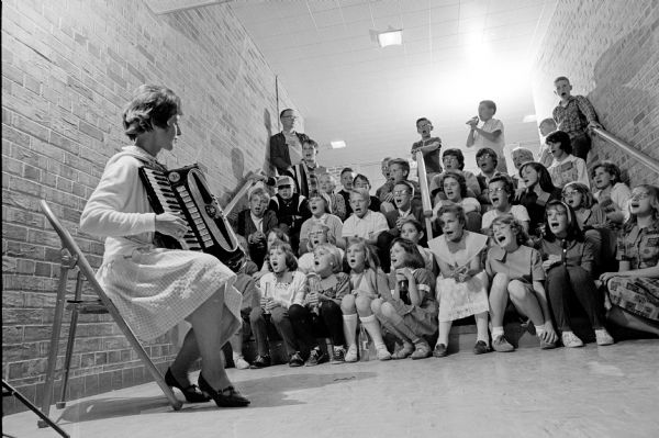 Volunteer Betty Faulkner plays an accordion while leading folk singing with children and parents at Gompers School as part of a YWCA program for 10 to 14 year old children.
