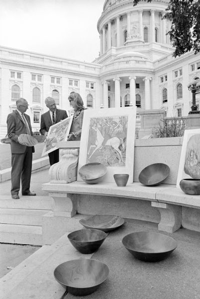 The Madison Art Association's 2nd annual Downtown Sidewalk Art Fair is held on the Capitol grounds. Shown admiring art work to be displayed is Governor Warren Knowles (center) with wood artist Harry Nohr, Mineral Point (L), and etching artist Jane Marshall Brewer, 3340 Gregory Street.