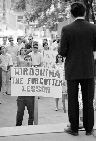 University of Wisconsin-Madison student holding a placard in front of a speaker at a demonstration at the Wisconsin State Capitol commemorating the atom bombing of Hiroshima, Japan. The demonstration turned into a civil rights and get-out-of-Viet Nam rally.