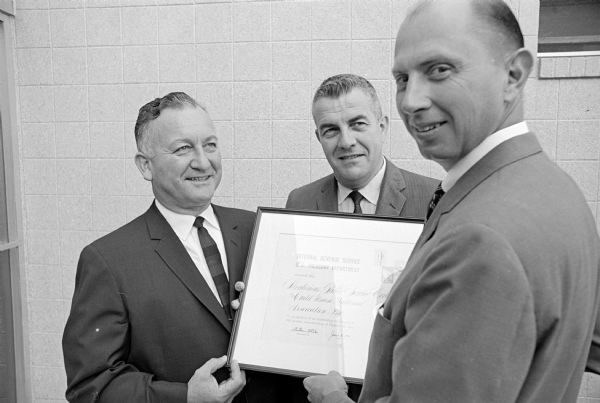 Three men posing with a plaque. The original caption states: "An award for meritorious public service was presented to CUNA International officials by W.S. Stumpf, right, district director of the Internal Revenue Service, Milwaukee. Receiving the award, based on creativeness, ingenuity, initiative, originality, and planning, were J. Orrin Shipe, managing director of CUNA International, and Kenneth Marin, president of CUNA."