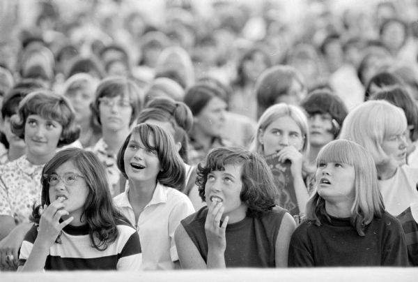 Audience members at a pop-concert-fashion show held by the Gimbels-Schusters department store outside the store in the Hilldale Shopping Center. Performance of hit-parade songs was performed by singers Peggy March and Bernie Thomas who were backed-up by the musical group DuPont dance group. Interspersed between the songs was a fashion show by the "Gimbelteens," representatives of area high schools. About 1,000 young people attended the concert-fashion show.