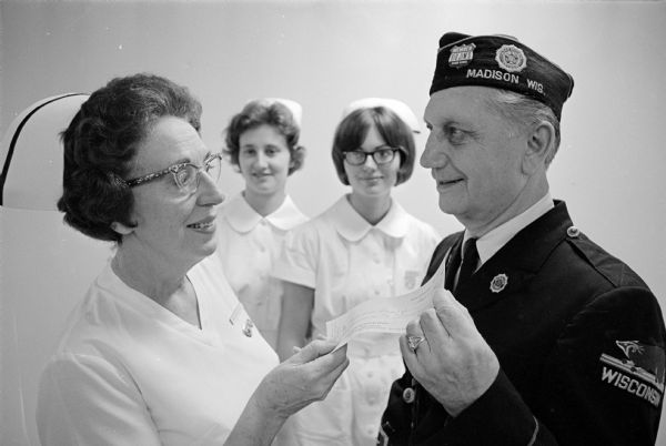 Ben Bergor presenting a check to Ann Geyer, director of nursing at Methodist hospital, that comes from the profits of the Kitty Wells show sponsored by the Dane County Council of the American Legion. The donation is to aid nursing students. Looking on are two student nurses, Judith Godfrey from Mineral Point, and Lisbeth Haddon from Edgerton.