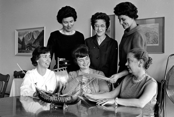 Faculty wives are shown making plans for Pentagon's luncheon and style show. Sitting left to right: Jean Stewart, Anita Gaggioli, and Jean Watson. Standing: Jane Kliebhan, Maureen Duchon, and Jane Loper.  Pentagon is the social organization of faculty wives of the University of WI College of Engineering.