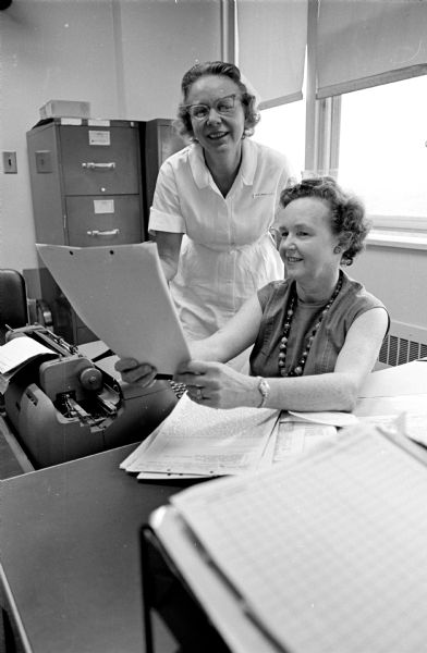 Indoor portrait of Orvella Jones (standing), a practical nurse, and Vera Neff, a hospital secretary. They were both employees of the Veterans Administration hospital and contributors to the Fair Share club of the United Givers Fund.