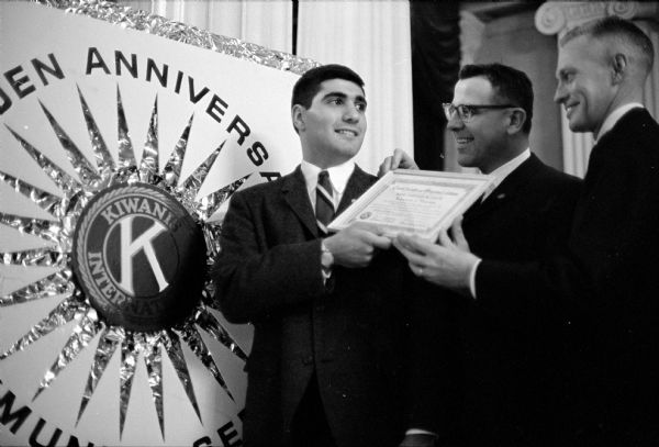 Paul Markos, president of the recently organized University of Wisconsin Circle K club, is shown accepting the organization's charter from Russell Williams, center, governor of the Wisconsin-Upper Michigan district of Kiwanis International. Gordon Johnson, president of the Downtown Kiwanis club, is on the right.