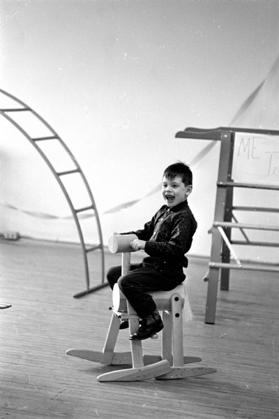 In a photograph advertising Creative Playthings, a young boy is sitting on a rocking horse, with climbing apparatus in the background. A catalog shop for Creative Playthings, educational and creative toys and equipment, is located on 2119 Atwood Avenue.