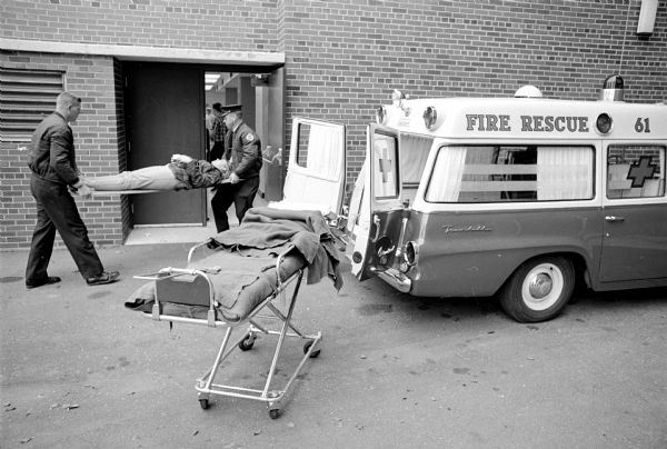 Participating in a practice disaster drill are two men carrying a "casualty" on a stretcher into an entrance to Madison General Hospital.
In this drill about 40 student nurses and high school students are taken to the hospital as simulated casualties of an airplane crash.