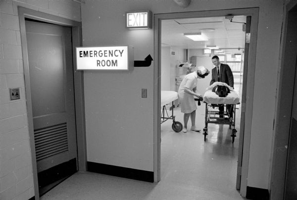 During a practice disaster drill, a nurse and a man are seen with a "casualty" on a stretcher at the Madison General Hospital emergency room. In this drill about 40 student nurses and high school students are taken to the hospital as simulated casualties of an airplane crash.