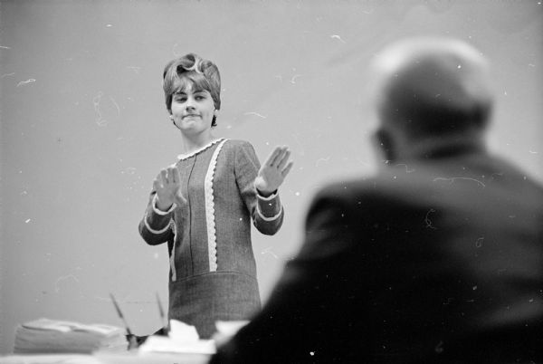 The Management Institute of the University of Wisconsin put on a seminar on leadership methods specifically for "Those Who Supervise Women Employes." It was well attended and two-thirds of the attendees were men. Image shows Madison Theater Guild actor Walter Malec sitiing in the right foreground, out of focus. Actress Dinah Felland (left), is standing with her hands forward in resistance. The original caption states: "Offer them a promotion and they say 'no thanks!'" One of the conclusions of the seminar was women place home obligations first and men place work obligations first.