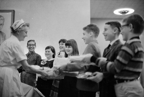 Hanukkah, the Jewish Festival of Lights, begins at the Temple Beth El. Sixth graders from the temple start the festival by giving gifts to children in the University Hospital. Miss Anna Thiessen, staff nurse at the hospital, is shown accepting the presents from, (L-R): Ron Salomon, Lorie Druck, Janice Wexler, Shelly Dutch, David Conney, Jeff Sachs, and David Blotner.    