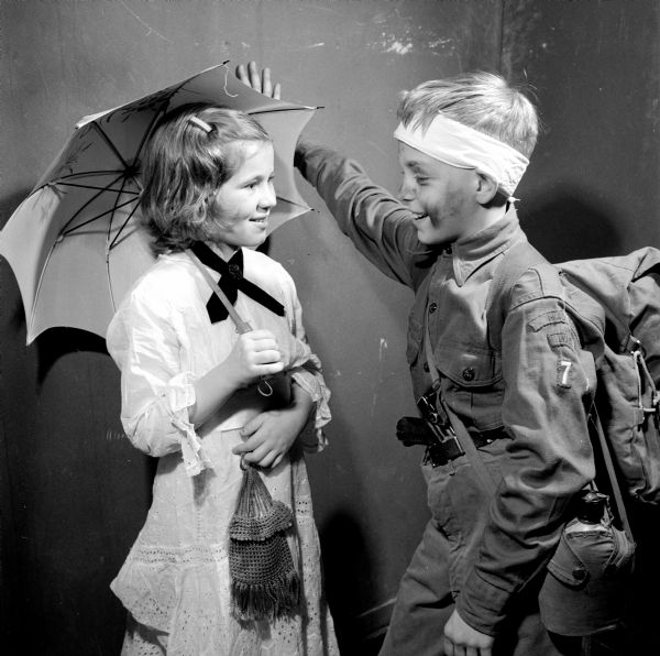 Boy Scout from Troop 7, wearing uniform, backpack and canteen, looking at a girl in an old-fashioned costume, carrying an open umbrella.