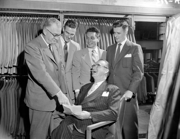 Ad for WMTV showing Roundy Coughlin signing a contract with The HUB, his TV sponsor.  Pictured with Roundy are Ed Schmitz, Jim Schmitz and Bob Schmitz, owners of The Hub, a men's clothing store, and Jerry Bartell, second standing person from the right, owner and manager of WMTV.