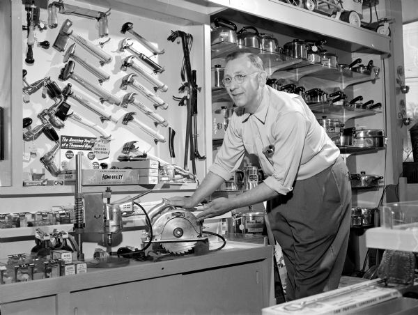 Henry Vetter pointing to a small table saw in front of a display of hardware in his store in the Shorewood Corners Shopping Center, 3234 University Avenue.