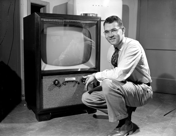 A man is crouching down and turning the dial on a television set in the Home of Television store near the Shorewood Corners Shopping Center, 3301 University Avenue.