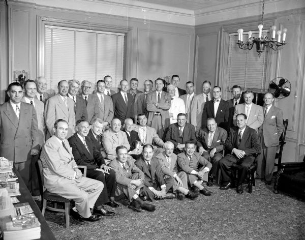Walter Meanwell is sitting in the middle of the first row holding a trophy surrounded by many former Wisconsin basketball players who gathered at the Madison Club to honor the U.W. basketball coach. Dr. Meanwell is generally credited with inventing the short pass system in basketball.
