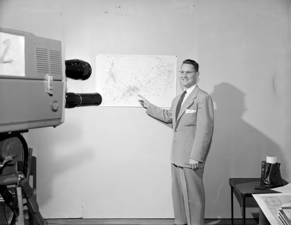 WMTV weatherman Paul Ekern is standing and pointing to a weather map in front of a WMTV television camera.