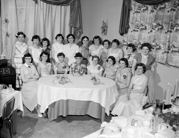 Slightly elevated view of a group of nineteen women standing and sitting behind a table, taken for Bess Weiner (?).