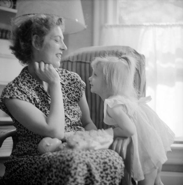 Indoor portrait of Mrs. Groth sitting and smiling at her daughter, with her daughter's doll on her lap.