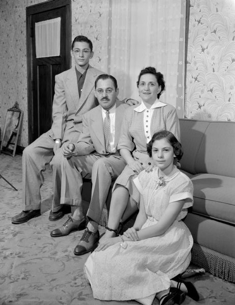 Group portrait of the Julius Mintz family. The father and mother are sitting on the couch, the son is sitting on the far left on the arm of the couch, and the daughter is sitting on the floor in the foreground on the far right.