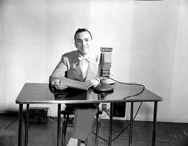 Portrait of John B. Davis, WKOW news editor, sitting at a table behind a microphone.