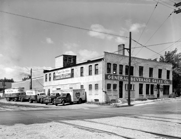General Beverage Sales Co., 114 N. Murray Street, with a Pabst Blue ribbon sign on the building and four trucks parked beside it. Railroad tracks run across the street in the foreground.