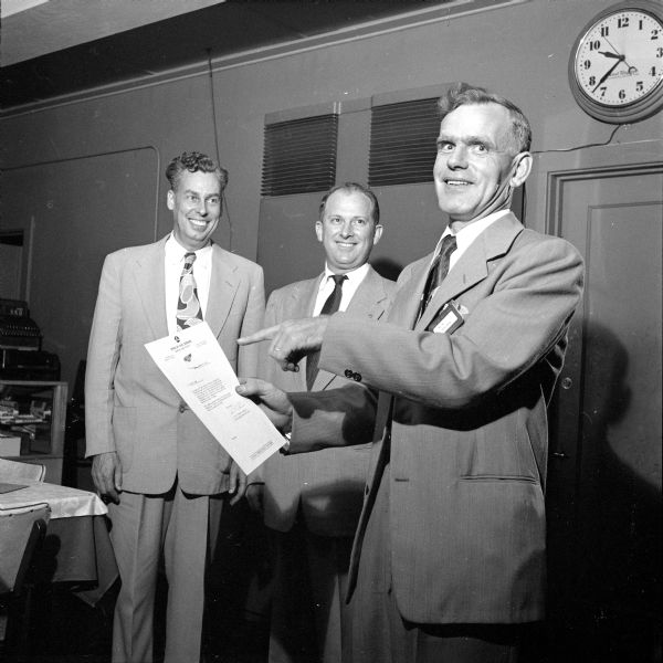Elton Hodge is pointing to his certificate and his badge of office as Dane County Defense Director while I.G. Trowbridge (left) and John F. Whitmore, club publicity director, look on. This was a special meeting to honor members of the organization who have won their wings in Madison's Ground Observer Corps, a civil defense group operating under the direction of the Air Force.