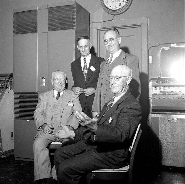 Charles Waddell (right) telling a story while, (left to right): Dr. William T. Lindsey, Harry Hayes and Henry Esser are looking on at a meeting of the South Side Men's Club. A large furnace and a cigarette machine are located behind the men.