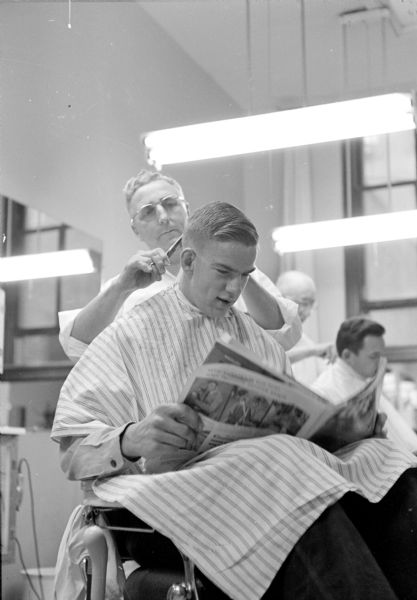 Tom Morrow reading a magazine while getting a haircut by barber Juell Solberg at the Union Bus Station barbershop.