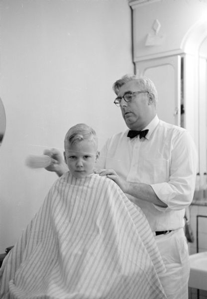 Barber Henry Palan cutting the hair of Billy Mayer in the Park Hotel barbershop.