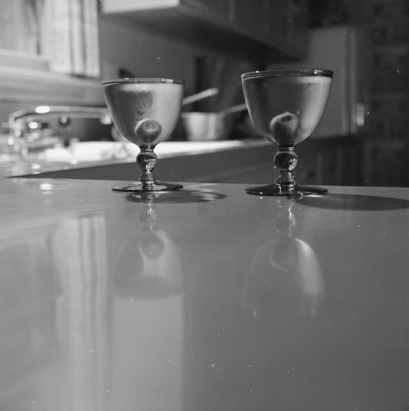 Two full Martini glasses with olives are sitting on a kitchen counter.