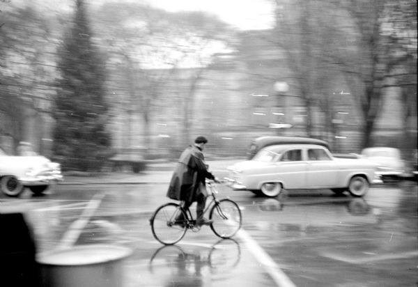 A person is bicycling around Capitol Square in the rain. 