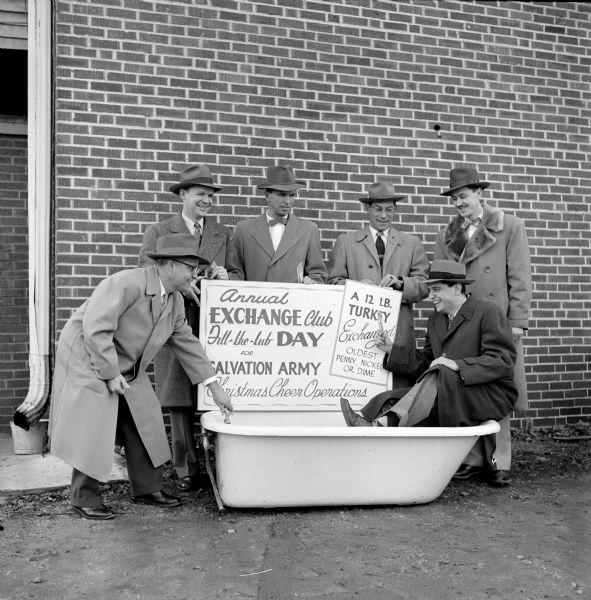 Members of the Madison Exchange Club with one of five bathtubs they will have around Madison to collect money for the Salvation Army Christmas baskets for needy families. One of the signs reads, in part: "Annual Exchange Club, Fill-the-tub Day for Salvation Army Christmas, Cheer Operations."