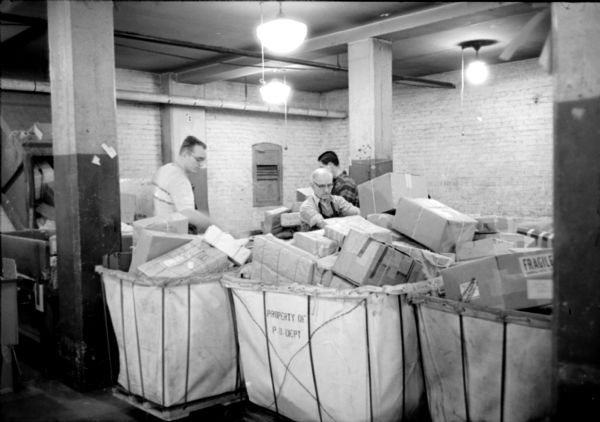 Postal workers (left to right): Robert Clark, Fred Boyd, and Donald O'Leary, are loading outgoing parcels and packages at the United States Post Office on Monona Avenue.  