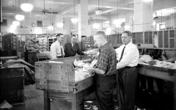 Monitoring the outgoing mail are (left to right): William C. Davis, assistant superintendent, George Gauke, superintendent, and William Vaeble. They are in the sorting room of the United States Post Office on Monona Avenue. 